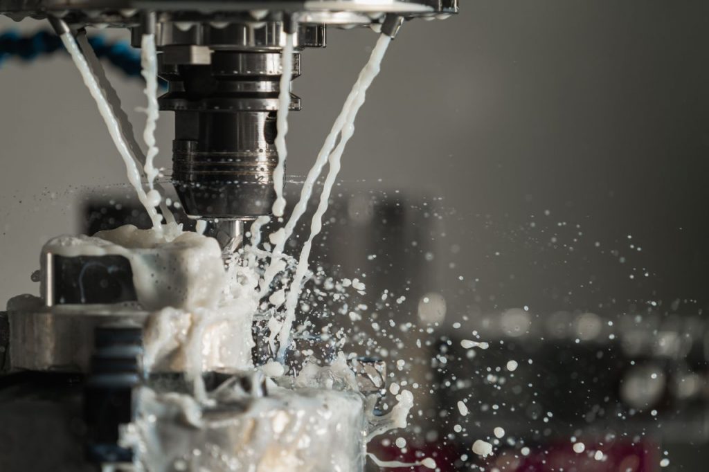 Dynamic close-up of CNC machine with coolant splashing during metalwork operation.